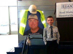 contributed photo Chase Rajkowski proudly stands next to a photo of his father, Ron, at a "Road Workers Memorial Event" in the Twin Cities. Ron was killed when a driver veered into him and a co-worker when they were working in a construction zone. Ron's wife, Jodi, was instrumental in getting stricter laws passed regarding work-zone driving violations.