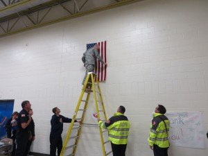 photo by Cori Hilsgen Major John Donovan positions the restored flag on the Colts Academy wall while fire department members and others watch. 