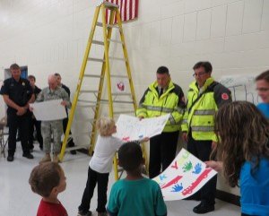 photo by Cori Hilsgen Children give thank-you posters to Major John Donovan and fire department members during the flag ceremony held Oct. 14 at Colts Academy.