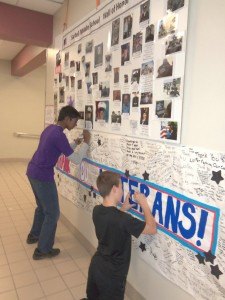 photo by Dennis Dalman Sartell Middle School students Janagan Ramanathan (left) and Thomas Ellis sign a banner under photos of military veterans displayed in the SMS lunchroom. The photos are of veterans who are related in some way to SMS students, who invited the veterans for a free lunch at the school for Veterans Day. It was the eighth annual such event at the school. 