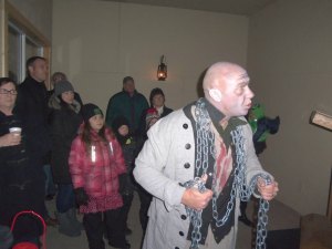 photo by Dennis Dalman Festooned in heavy chains, the ghost of Jacob Marley returned to haunt his former business partner, the mean-spirited tightwad Ebenezer Scrooge. Behind Marley are visitors to the walk-a-long theatrical event entitled Ebenezer at The Living Waters church in Sartell. 