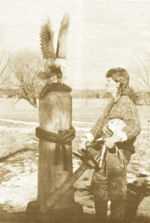 photo by Stuart Goldschen Chainsaw Man Mark Kurtz, with chainsaw and protective hockey helmet, admires his 8-foot sculpture of an eagle grasping a walleye on a rope-tied pier post in Avon. The sculpture is an example of Kurtz's popular chainsaw wood art.