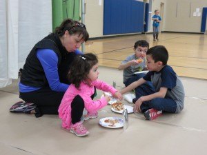 photo by Logan Gruber Jessie Sandoval, left, sits down with her children for some pizza, courtesy of the Gary's Pizza booth at the St. Joseph Community Showcase April 11 at Kennedy Community School. Many people made mention that the pizza, pie, and other treats served at the showcase were quite large portions, rather than sample sizes. Pictued with Jessie are her children, Natalia, 4, Andres, 6, and Amado, 9. Not pictured is Jessie's husband, Jesús Sandoval, who is a 7th  and 8th grade math teacher at Kennedy. Jesús was manning the St. Joseph Catholic Church booth at the showcase.