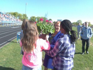 photo by Dennis Dalman Three middle-school girls present a huge planter of geraniums as a thank-you gift to departing Sartell Middle School Principal Julie Tripp during a rally May 21 at the football field. Students in the bleachers roared their approval.