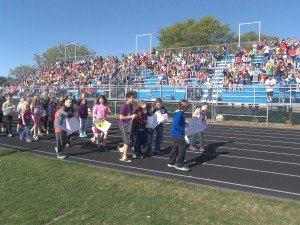 photo by Dennis Dalman Students carrying placards walk down the track to positions on the football field where they will surprise departing Sartell Middle School Principal Julie Tripp during a rally.