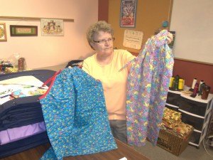 photo by Dennis Dalman Evelyn Kirchner holds up just two of the many dresses "The Quilters" make for little girls in an orphanage in poverty-stricken and earthquake-damaged Haiti.