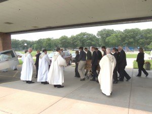 photo by Dennis Dalman Clergy line up outside as the casket of Sam Traut is brought by pallbearers to a waiting hearse for burial in St. Francis Xavier Cemetery. Traut was eulogized in the Burial Mass as a kind, helpful, hard-working Christian with a unique goofy sense of humor. 